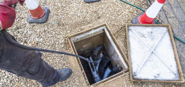 Man unblocking domestic sewage drain through open inspection chamber